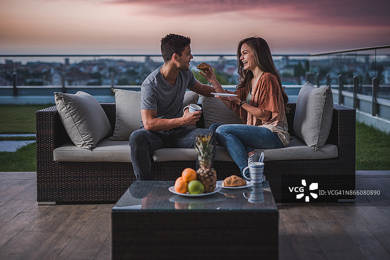 快乐的女人在顶层公寓的露台上喂她的男朋友图片素材