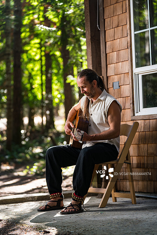 一名男子在林中小屋的露台上弹吉他唱歌图片素材