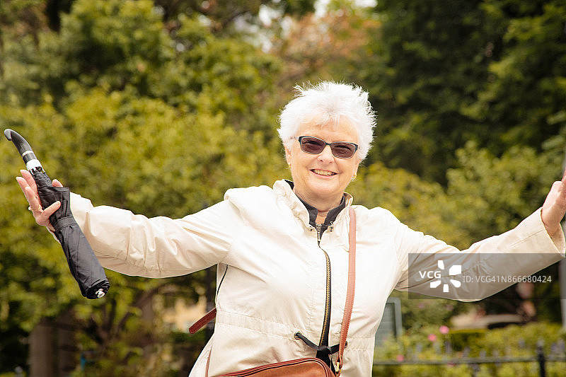 在公园里张开双臂微笑的年长妇女图片素材
