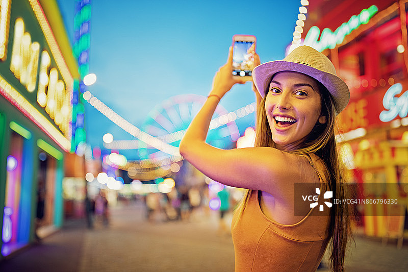 快乐的女孩在游乐场用手机拍照图片素材