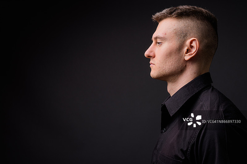 在灰色背景下穿着黑色衬衫的年轻英俊商人图片素材