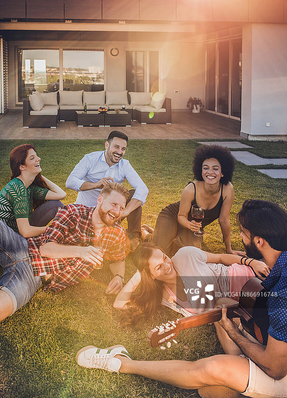 年轻人在房子前享受饮料和原声吉他图片素材