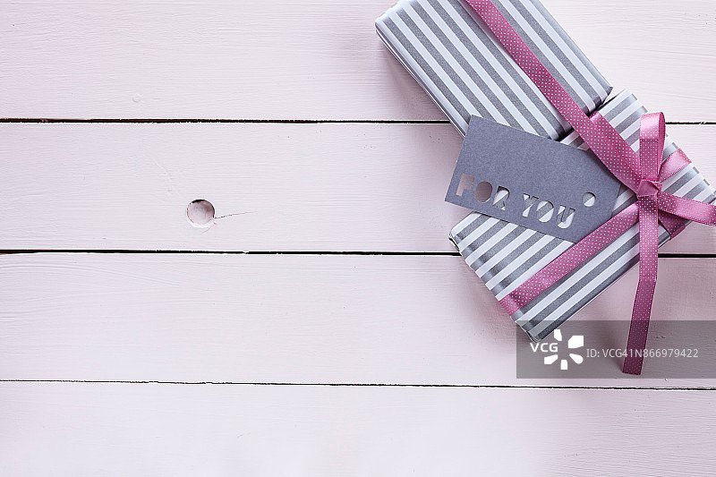 包裹在条纹纸、粉色丝带和标签上的礼品盒，位于涂成粉色的木制背景上。顶视图和复制空间。图片素材