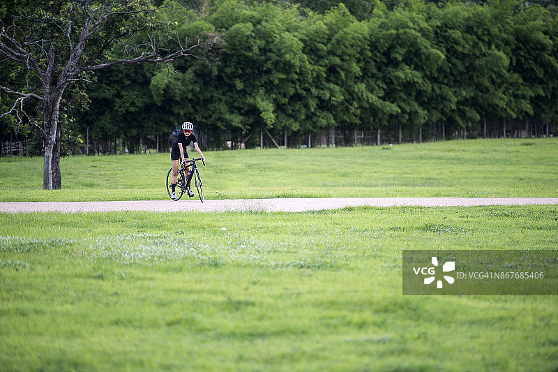戴头盔的亚洲健康女孩在自行车道上骑行锻炼图片素材