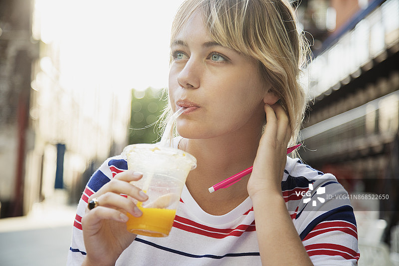 女人坐在城市广场的咖啡馆里喝新鲜的橙汁图片素材