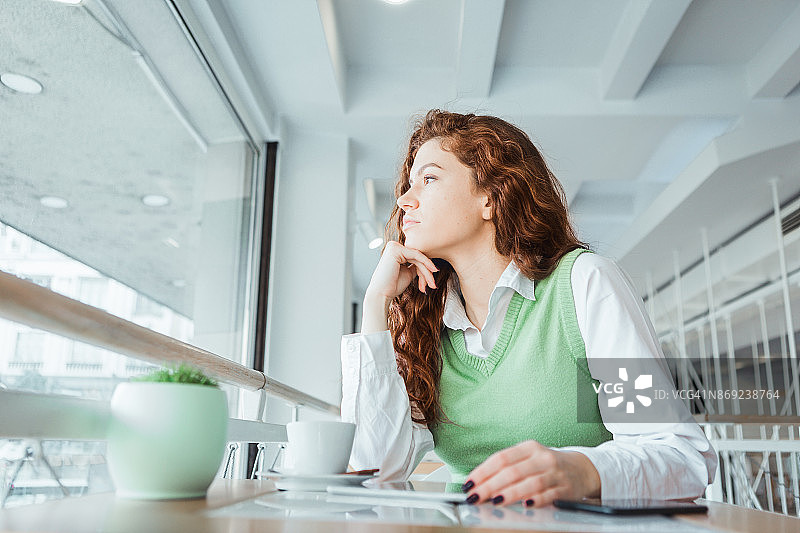 在咖啡馆喝咖啡、看平板的红色卷发女子图片素材