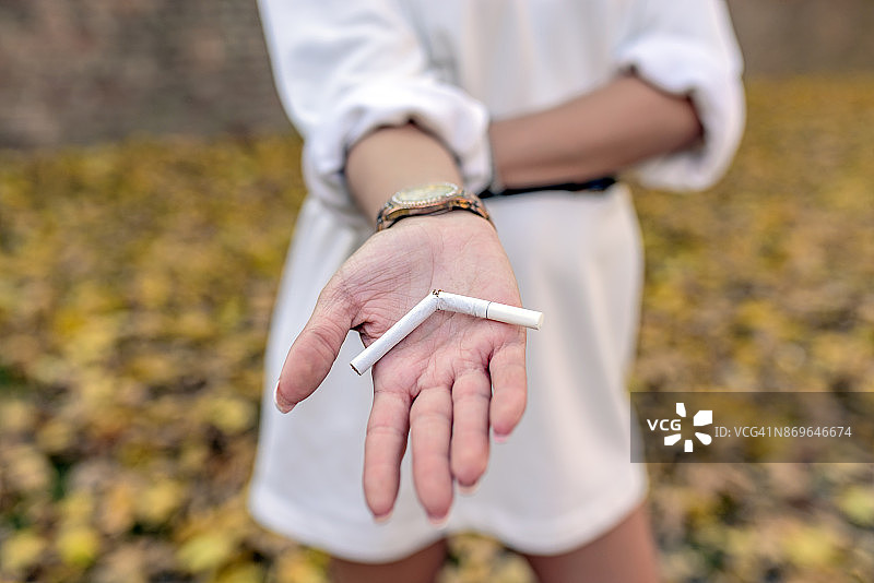 拿着断裂香烟的年轻快乐女子。停止吸烟概念。图片素材