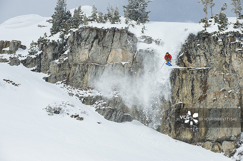 在阳光明媚的冬日，男人从悬崖上跳下，在粉雪上滑雪图片素材