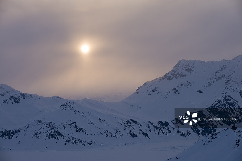 阳光穿过云层照耀在白雪皑皑的山脉上图片素材