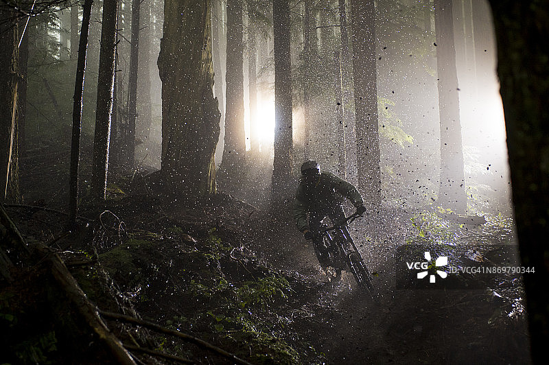 男人在雨中骑山地自行车穿过树林图片素材