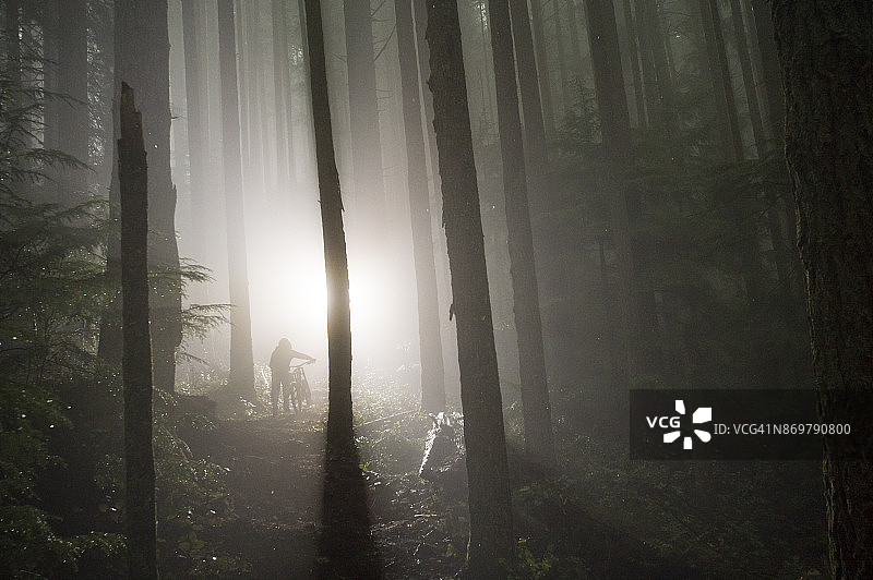 男人在雨中骑山地自行车穿过树林图片素材