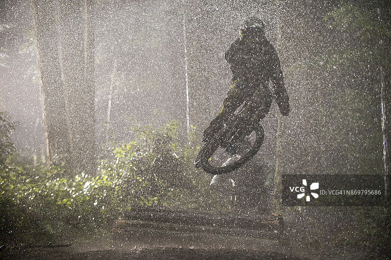 男人在雨中骑山地自行车穿过树林图片素材