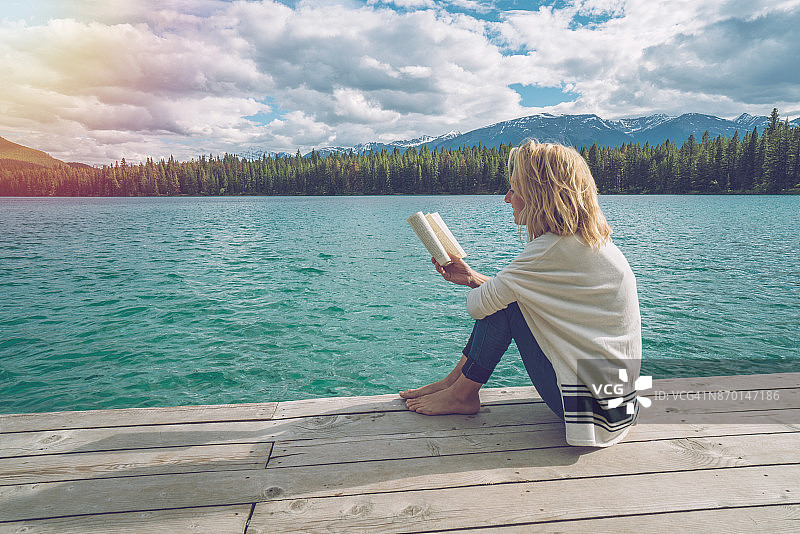在湖边码头上看书放松的年轻女子图片素材