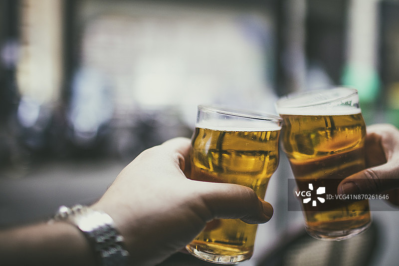 夫妇在巴黎咖啡馆酒吧的桌旁举着两杯啤酒庆祝图片素材
