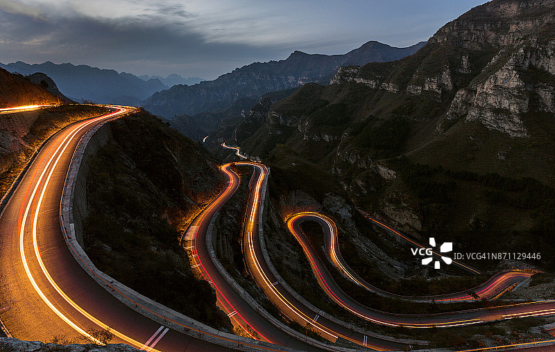 蜿蜒的道路在黄昏时分向上延伸，有发夹弯和交通灯图片素材