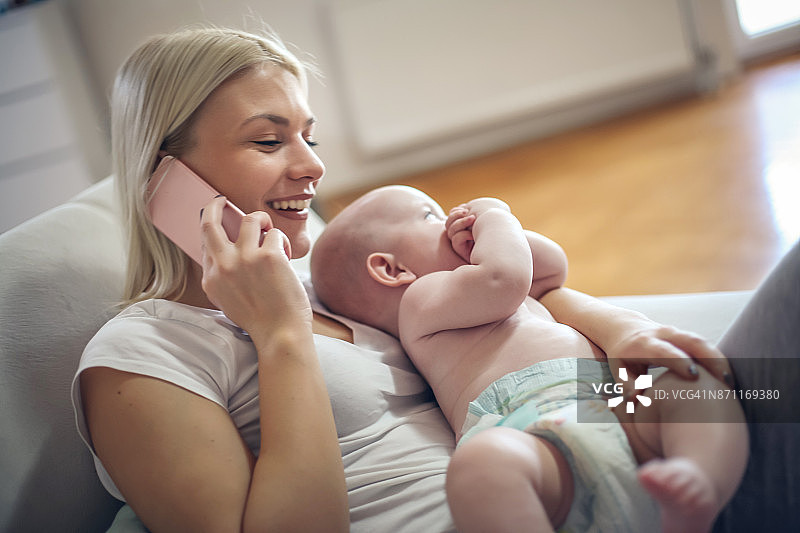 母亲抱着男婴，正在用手机交谈图片素材