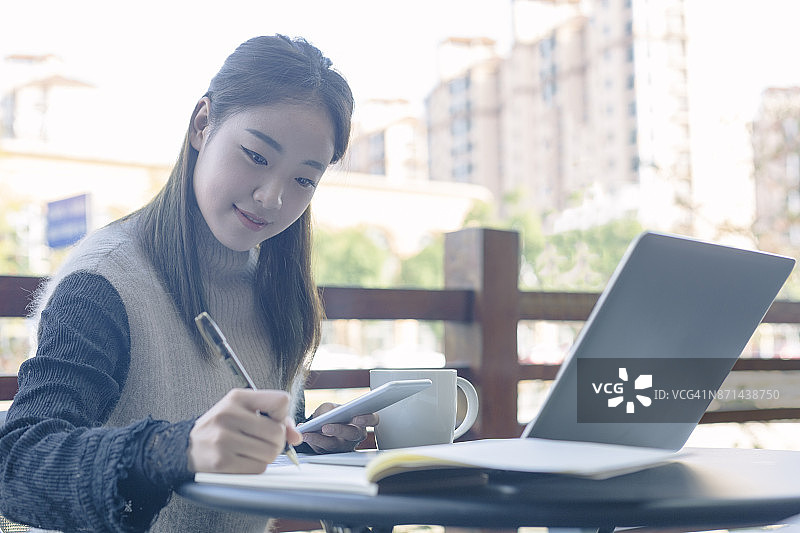 年轻女人拿着智能手机做笔记图片素材