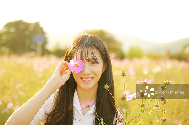 手持波斯菊花遮眼的女子肖像图片素材