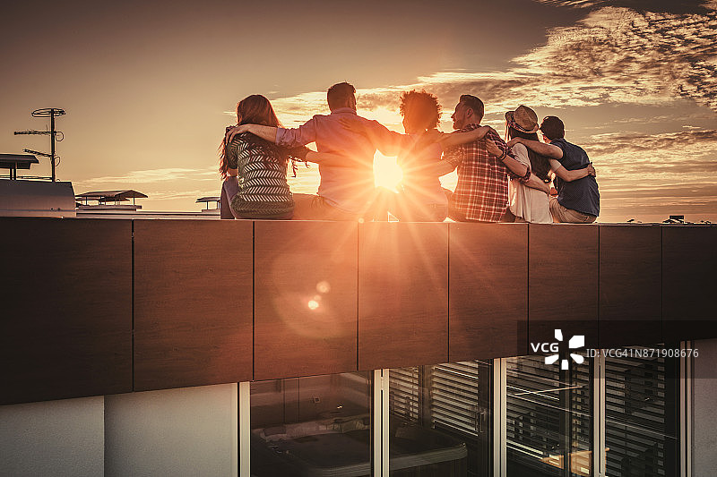 日落时分，朋友们在屋顶上放松拥抱的后视图图片素材