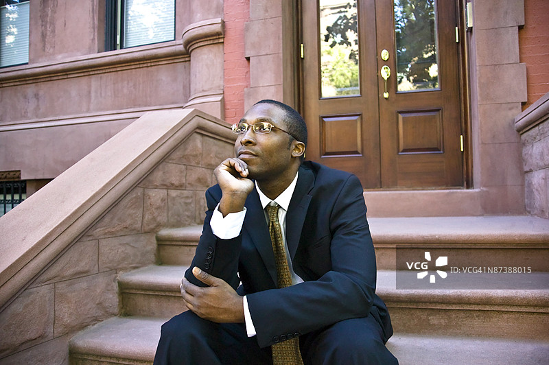 男人坐在纽约市哈莱姆区褐石建筑前图片素材