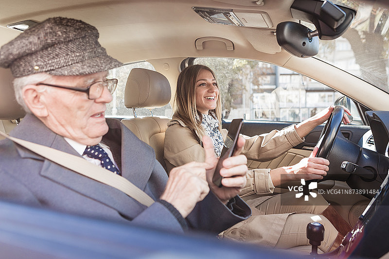 社交老人：祖父和孙女乘车兜风，祖父正在使用手机图片素材