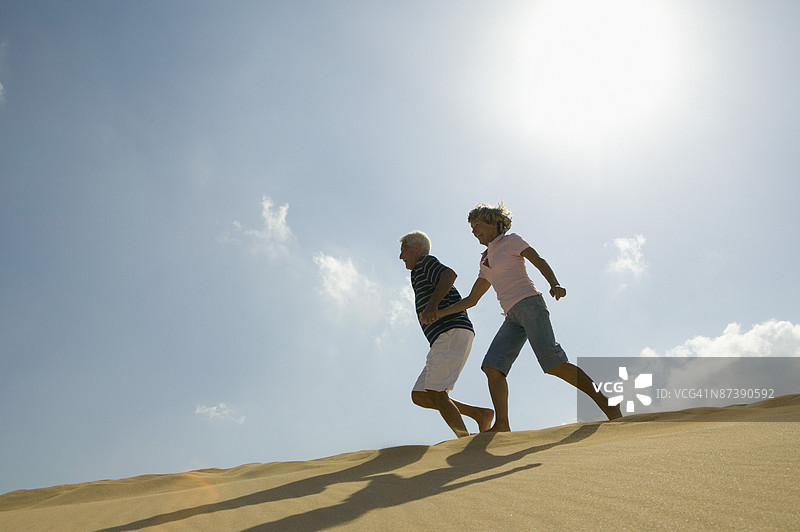 中年夫妇手牵手在海滩上奔跑图片素材