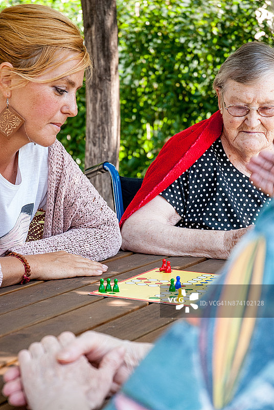 与女性看护一起玩飞行棋的老年妇女图片素材