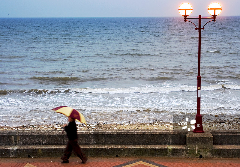 手持雨伞的女士在英格兰约克郡布里德灵顿海滨散步图片素材