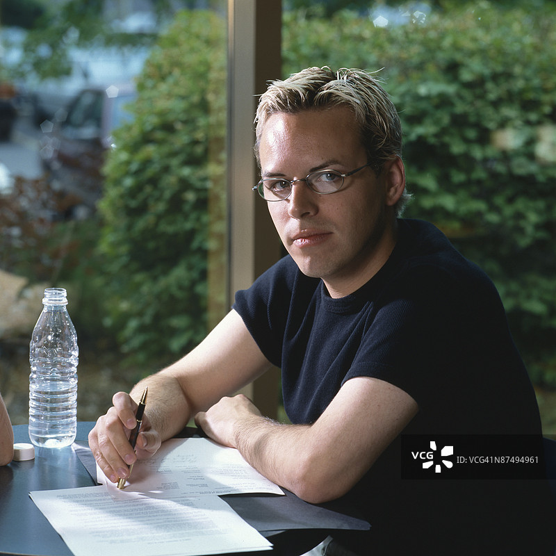 男子在桌子旁摆姿势，手边有文件图片素材