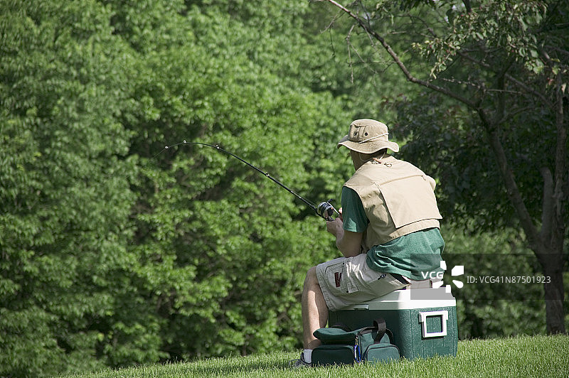 露营者坐在冷藏箱上钓鱼图片素材