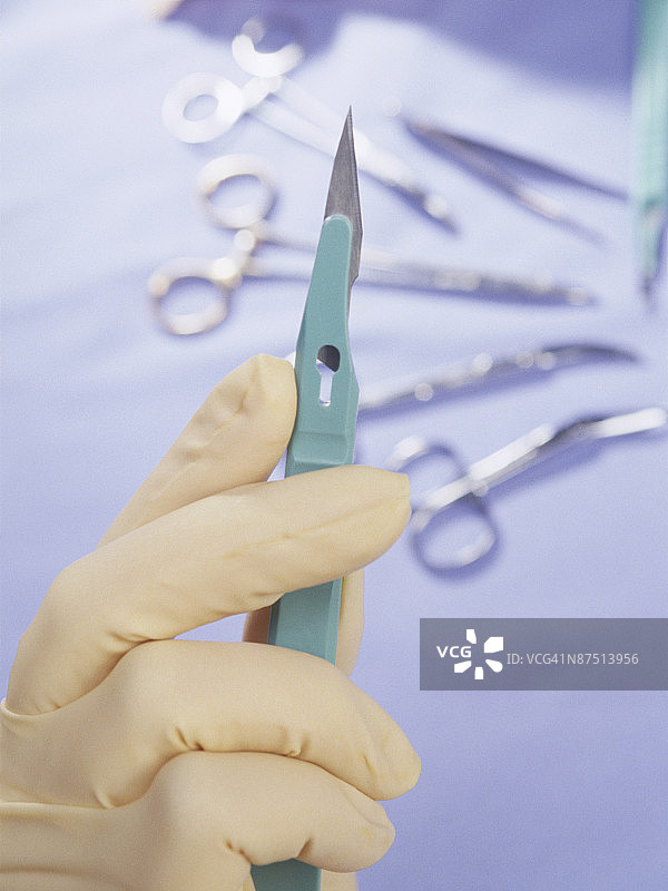 手持手术刀，背景有医疗器械图片素材