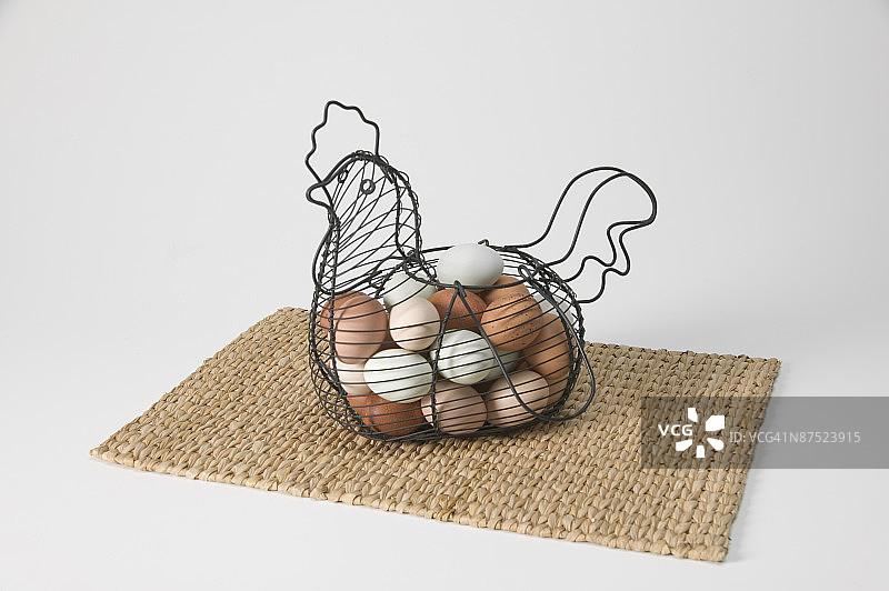 母鸡造型铁丝篮里的鸡蛋，置于餐垫上图片素材