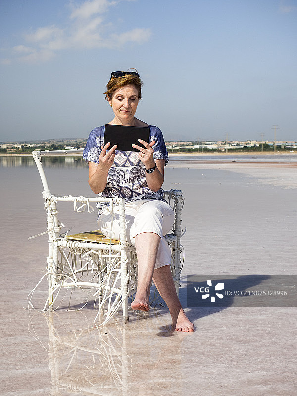 阳光下女人在湖边藤椅上阅读图片素材