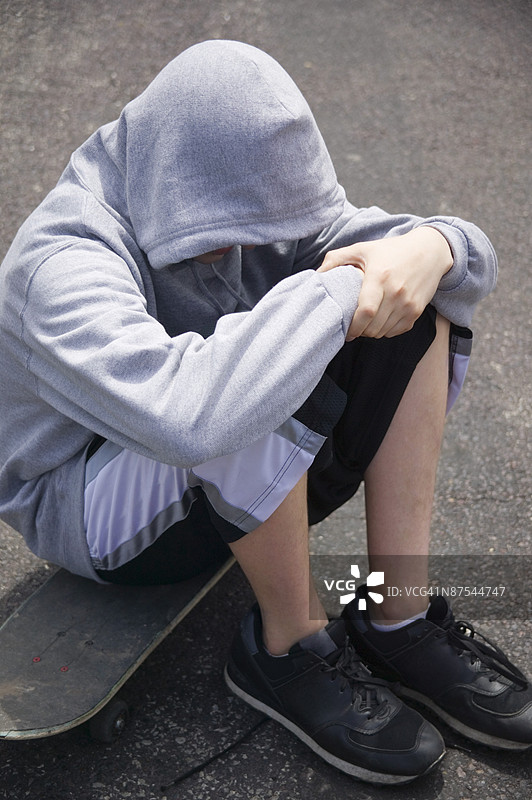 戴着兜帽的年轻人坐在滑板上图片素材