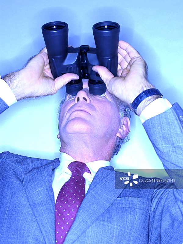 中年白人商人用双筒望远镜向上看图片素材