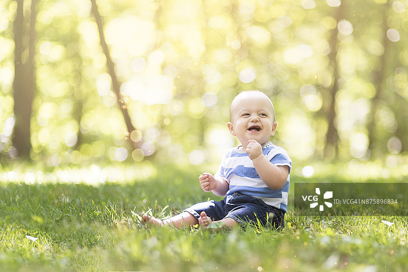 7个月大的异卵双胞胎男孩坐在草地上，沐浴在阳光下欢笑图片素材