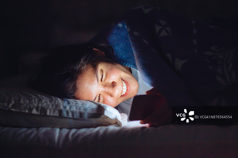 年轻女人在卧室的床上使用智能手机图片素材