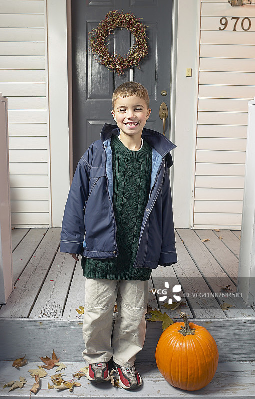 微笑的男孩站在门廊上，手拿南瓜图片素材