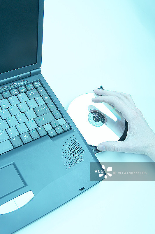 在笔记本电脑的磁盘驱动器中加载CD的人的摄影棚照片图片素材