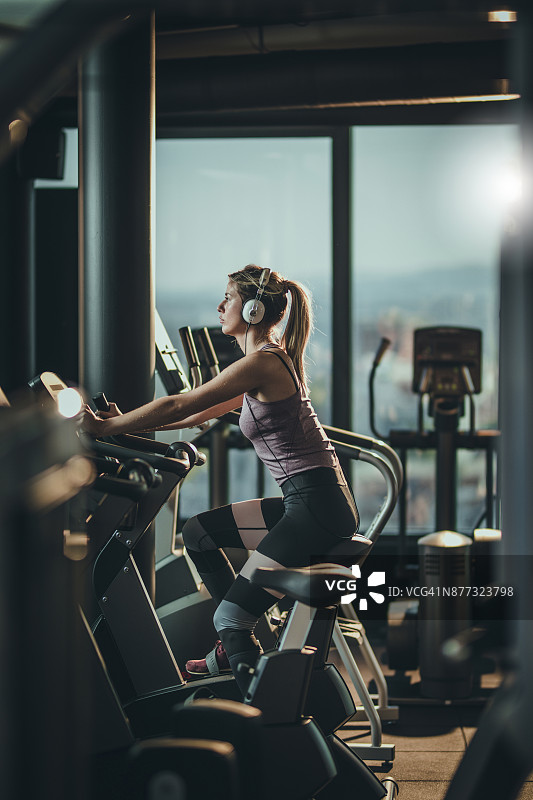 在健身房的动感单车上听音乐的健壮女人图片素材