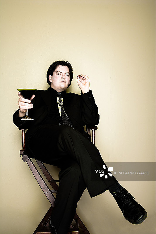 坐在椅子上抽着雪茄喝着鸡尾酒的傲慢男人图片素材