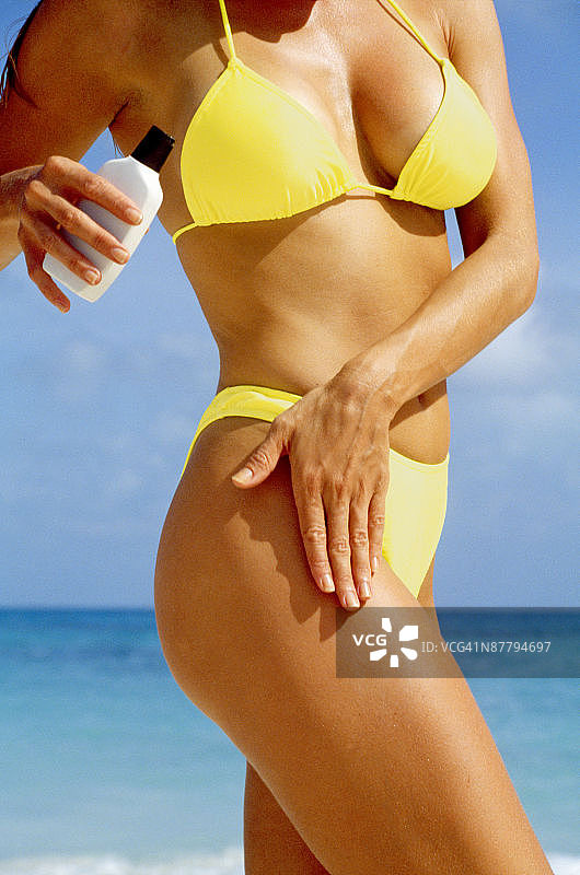 穿着比基尼往大腿上涂抹乳液的女人图片素材