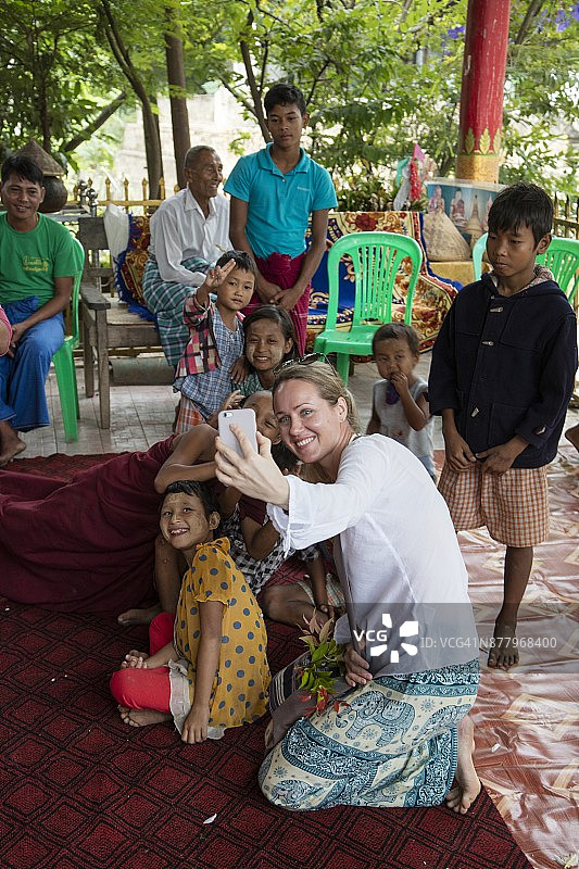 在缅甸曼德勒Tagaung村，阿耶亚瓦底江游轮Anawrahta号（Heritage Line）的客人与当地人在文化表演期间用iPhone自拍图片素材