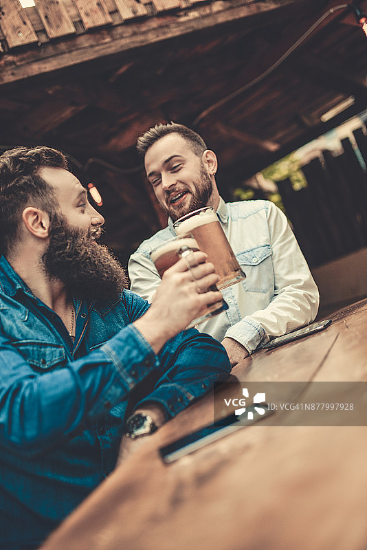 两个微笑的络腮胡男人喝着啤酒，玩得很开心图片素材