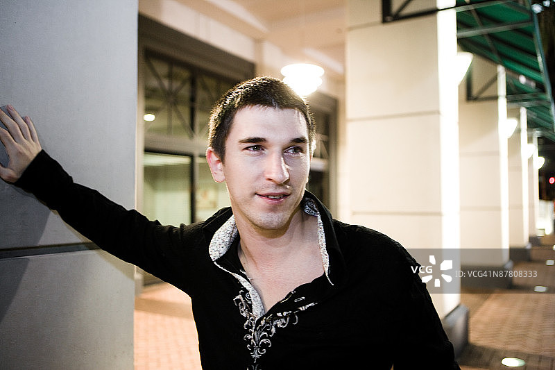 夜晚，男子倚靠在户外柱子上图片素材