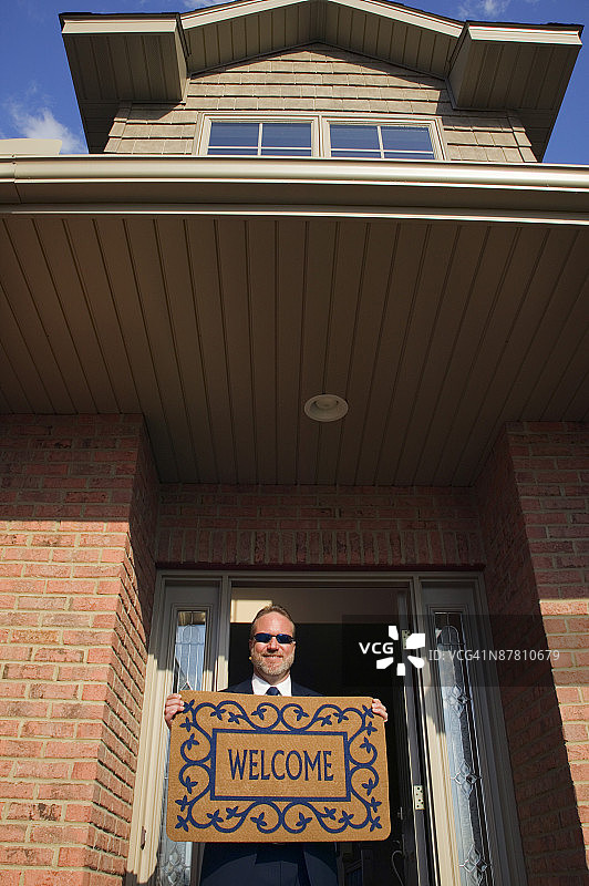 男子在房子前拿着欢迎垫图片素材