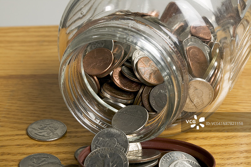 Jar of coins spilling on table图片素材