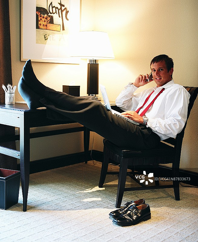 商人在酒店房间使用笔记本电脑和手机放松图片素材