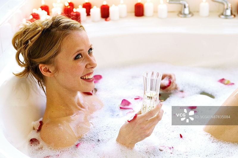 女人在泡泡浴中放松，手中拿着香槟酒杯图片素材