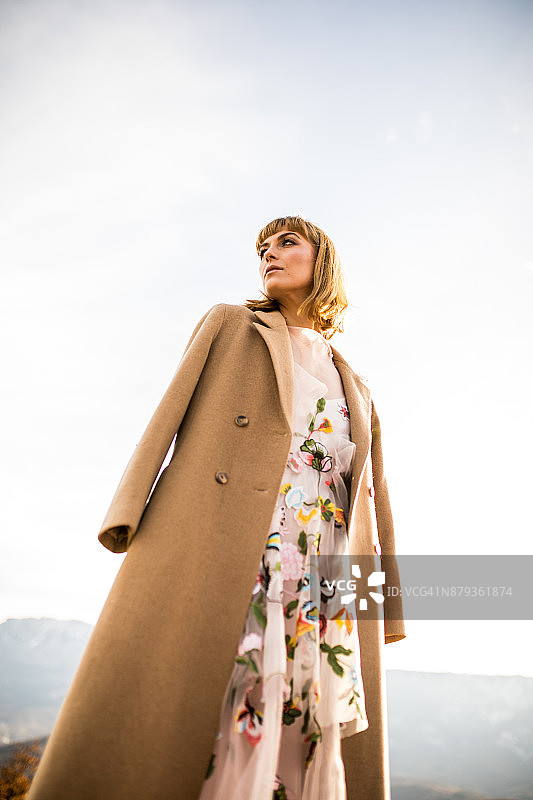穿着浪漫连衣裙和外套在田野里享受的年轻沉思女子图片素材
